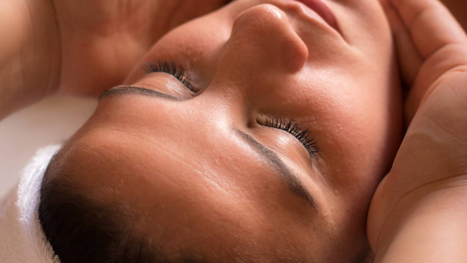 Close-up of woman with eyes closed facing up as hands cup her face and chin