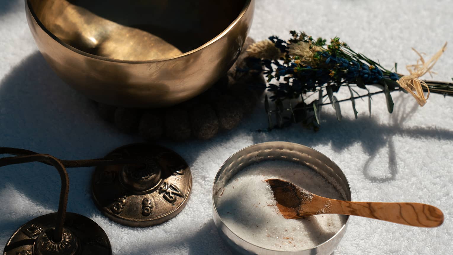 A small empty metal bowl, a small bundle of plants, a small bowl containing a whitish substance and a small spoon, and a set of small metal bells.