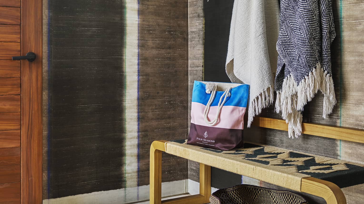 Resort room entryway with stylish wooden bench, shawls and hat hanging on wall hooks and a straw basket
