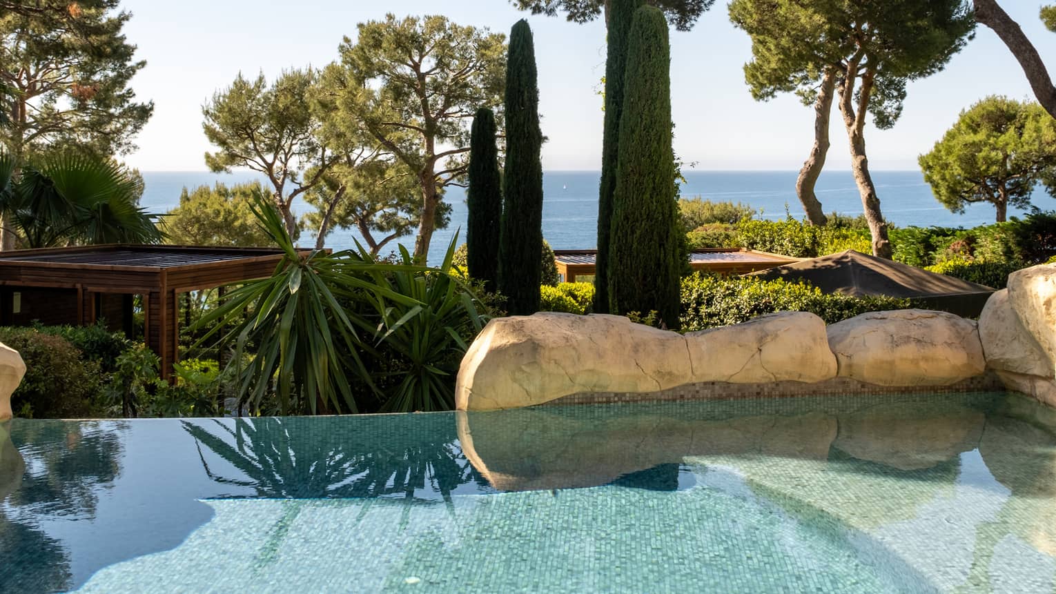 Pool surrounded by gardens with the sea in the distance