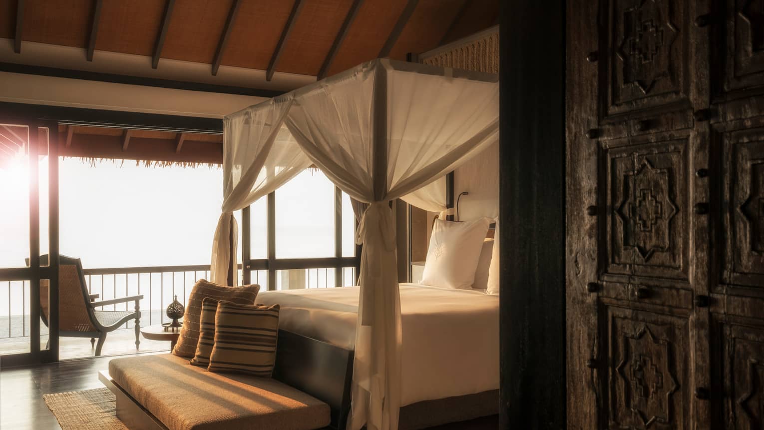Mezzanine Suites cushioned bench with pillow at foot of canopy bed with white curtains in sunlight