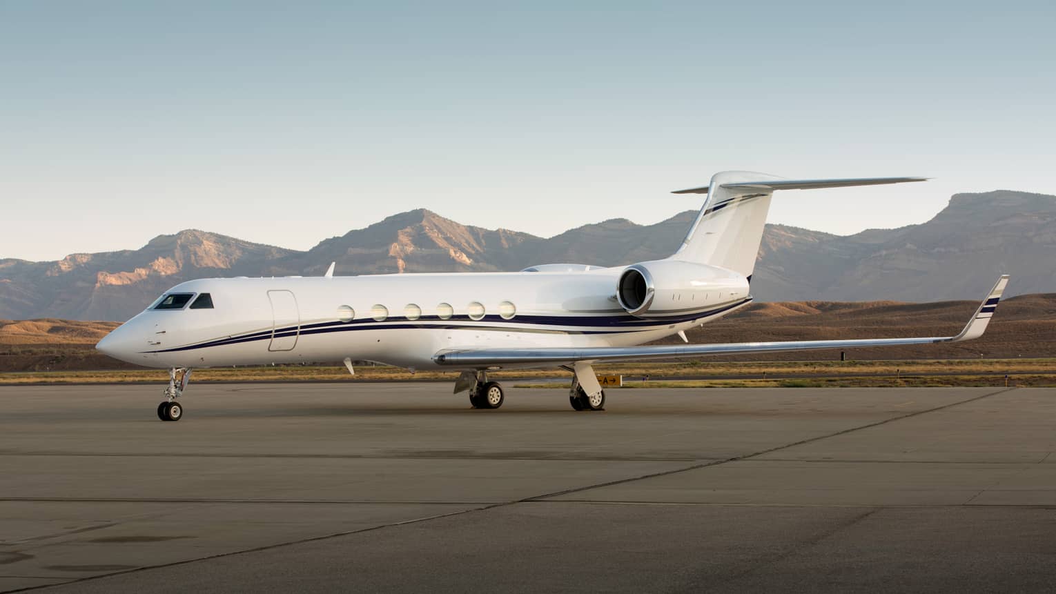 Private jet parked on a runway with mountain range in the background.