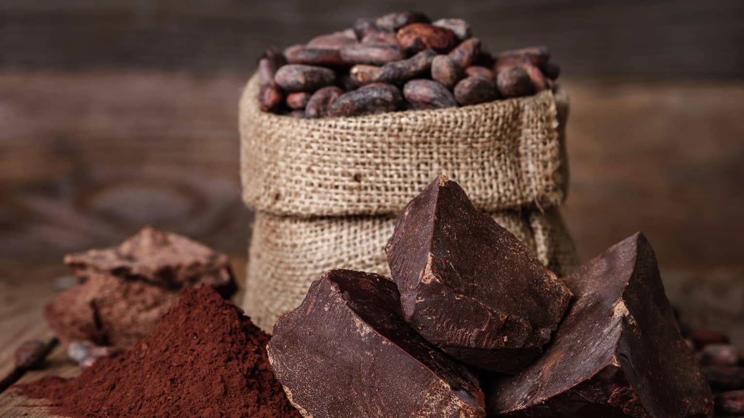 Chunks of chocolate, cocoa powder and coffee beans in a burlap sack