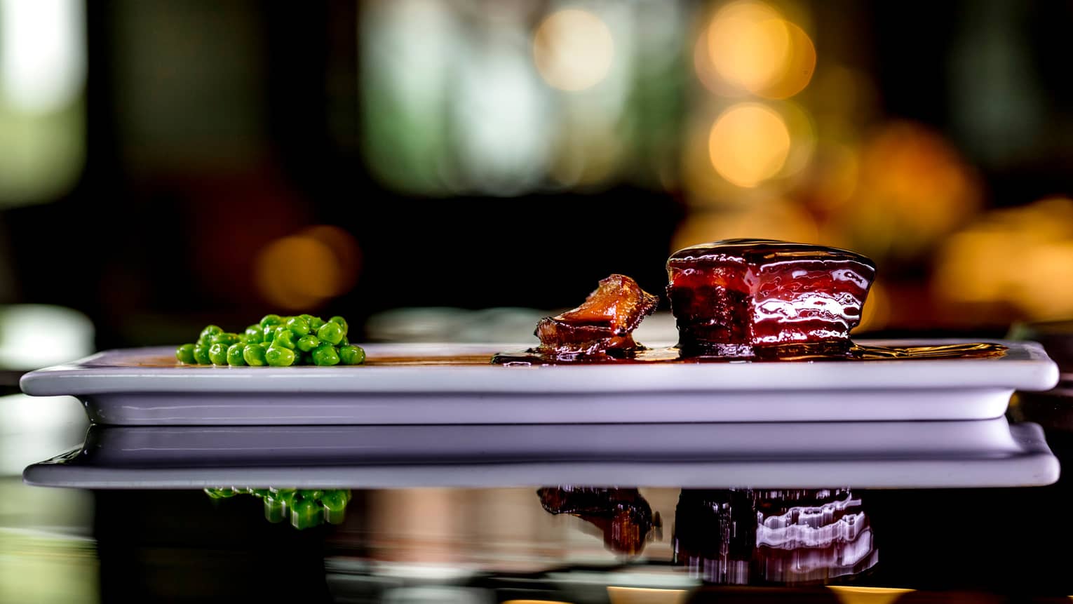 Side view of Shanghainese Braised Pork, peas on white platter 