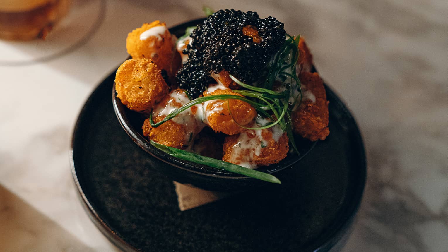 Caviar and fried potato on a small black plate.