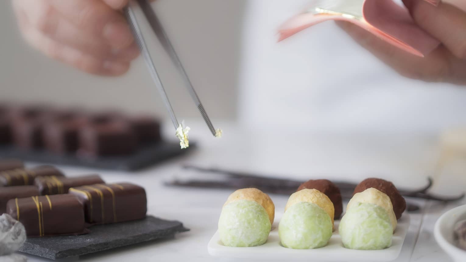 A close up of a male chef's hands using tongs to place various chocolates on parchment paper