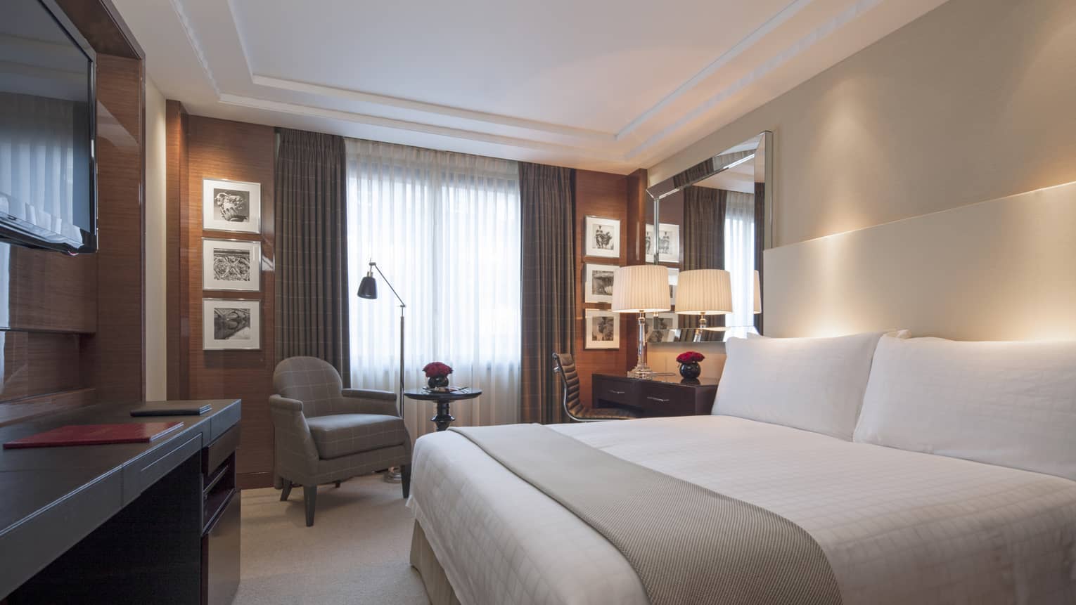 Superior Room bed with sash on white wall with accent lighting, armchair by curtains