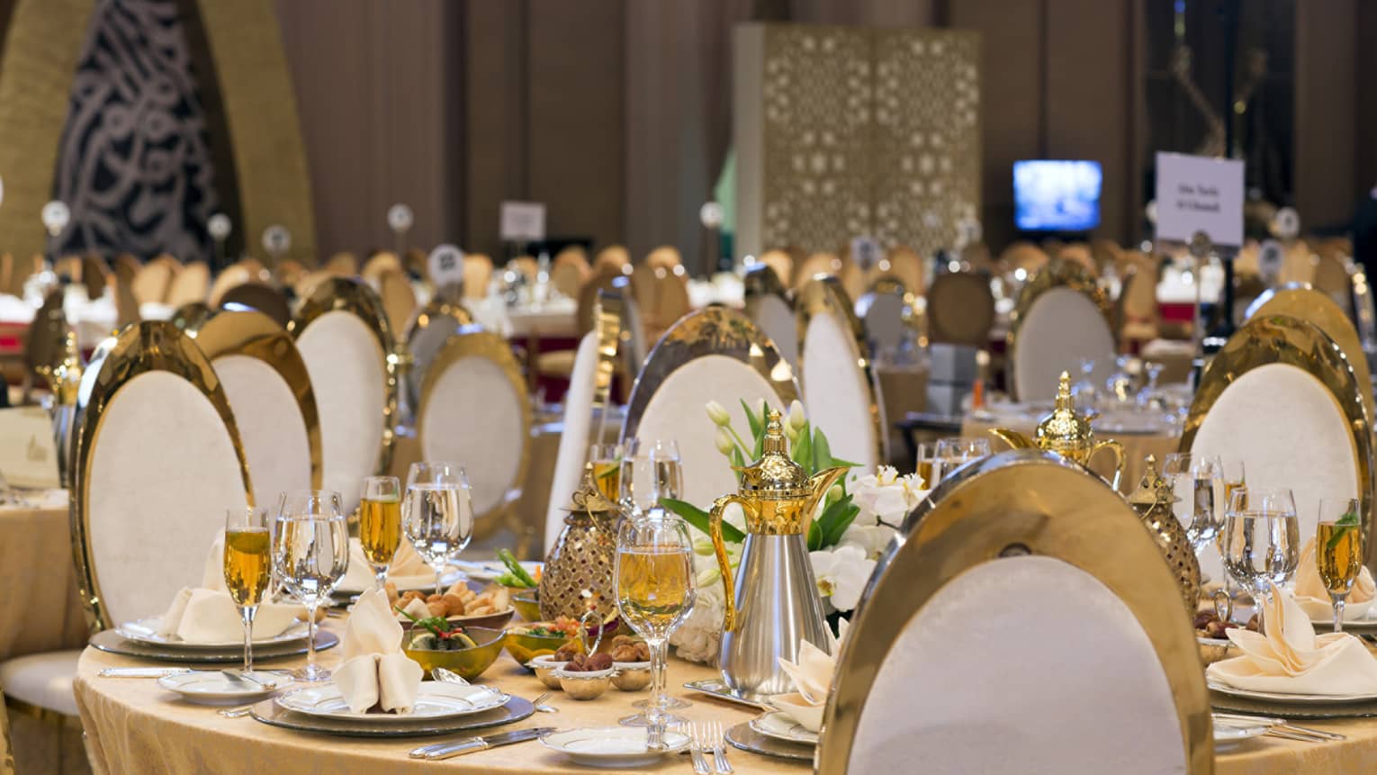 Round table set for dinner with wine glasses, flowers, napkins and white and gold chairs