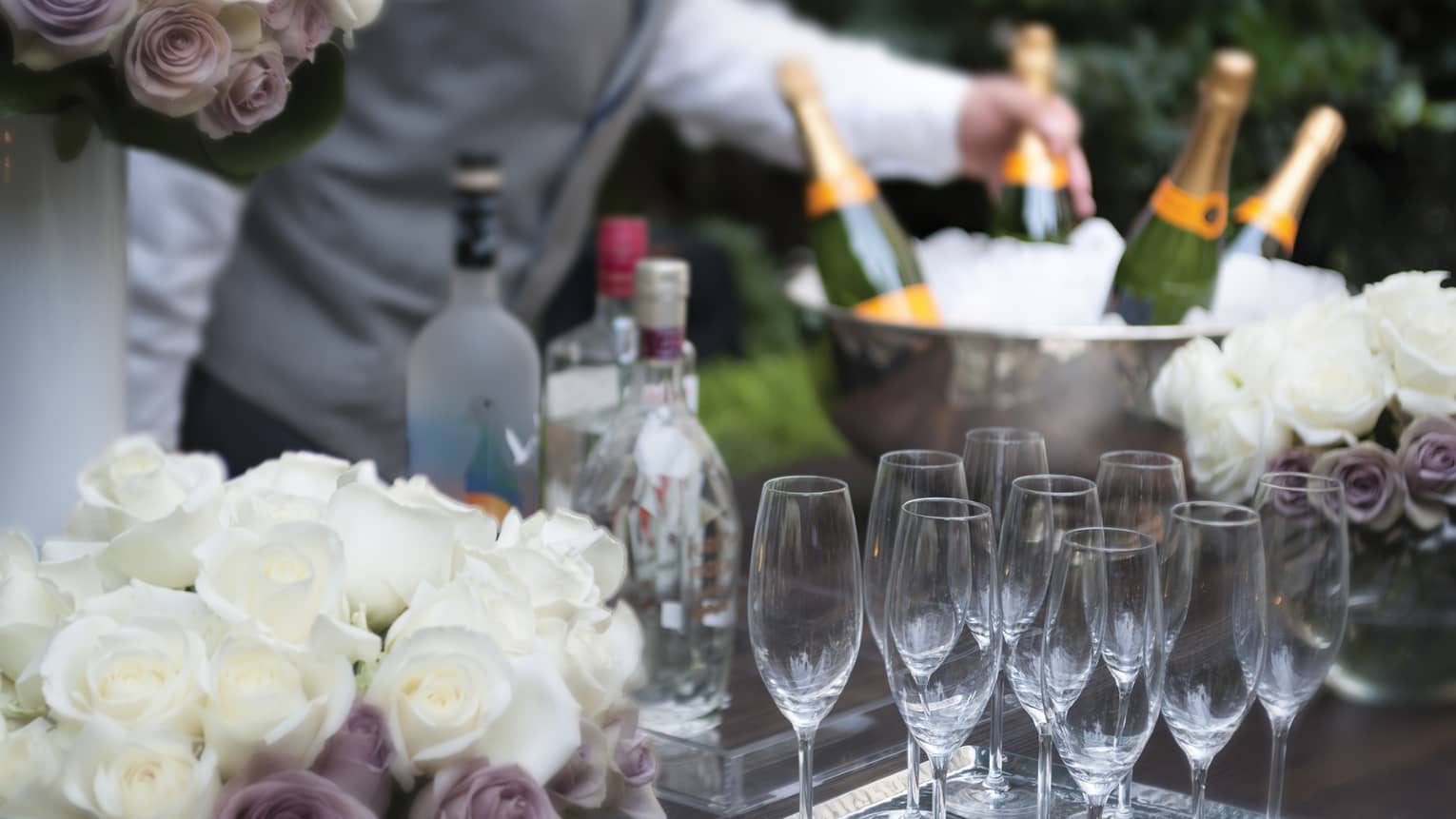 A table of white and lavender flowers and empty classes sit at a banquet cocktail set-up