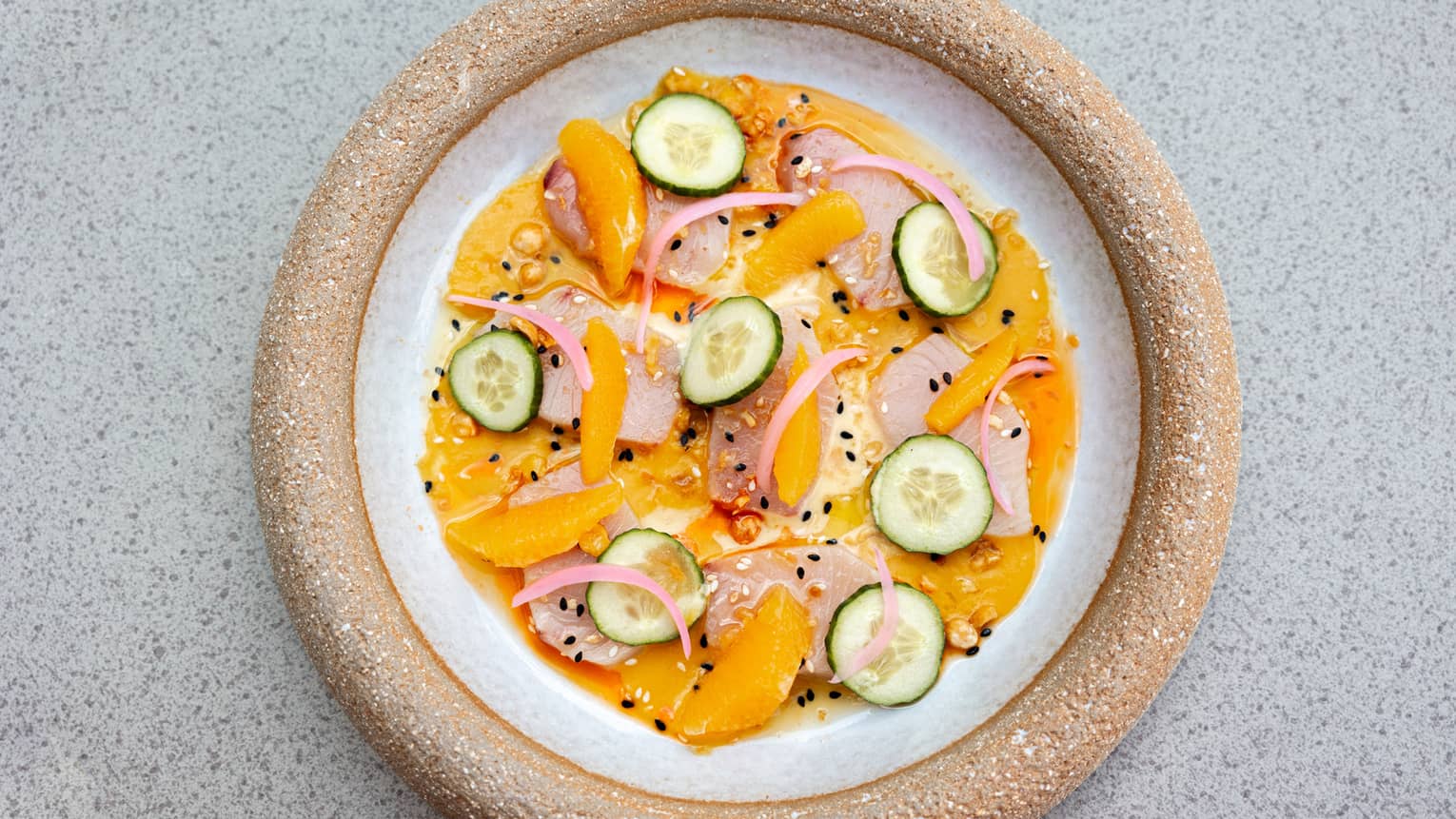 A round plate holds colourful food items, including citrus segments and cucumber slices.