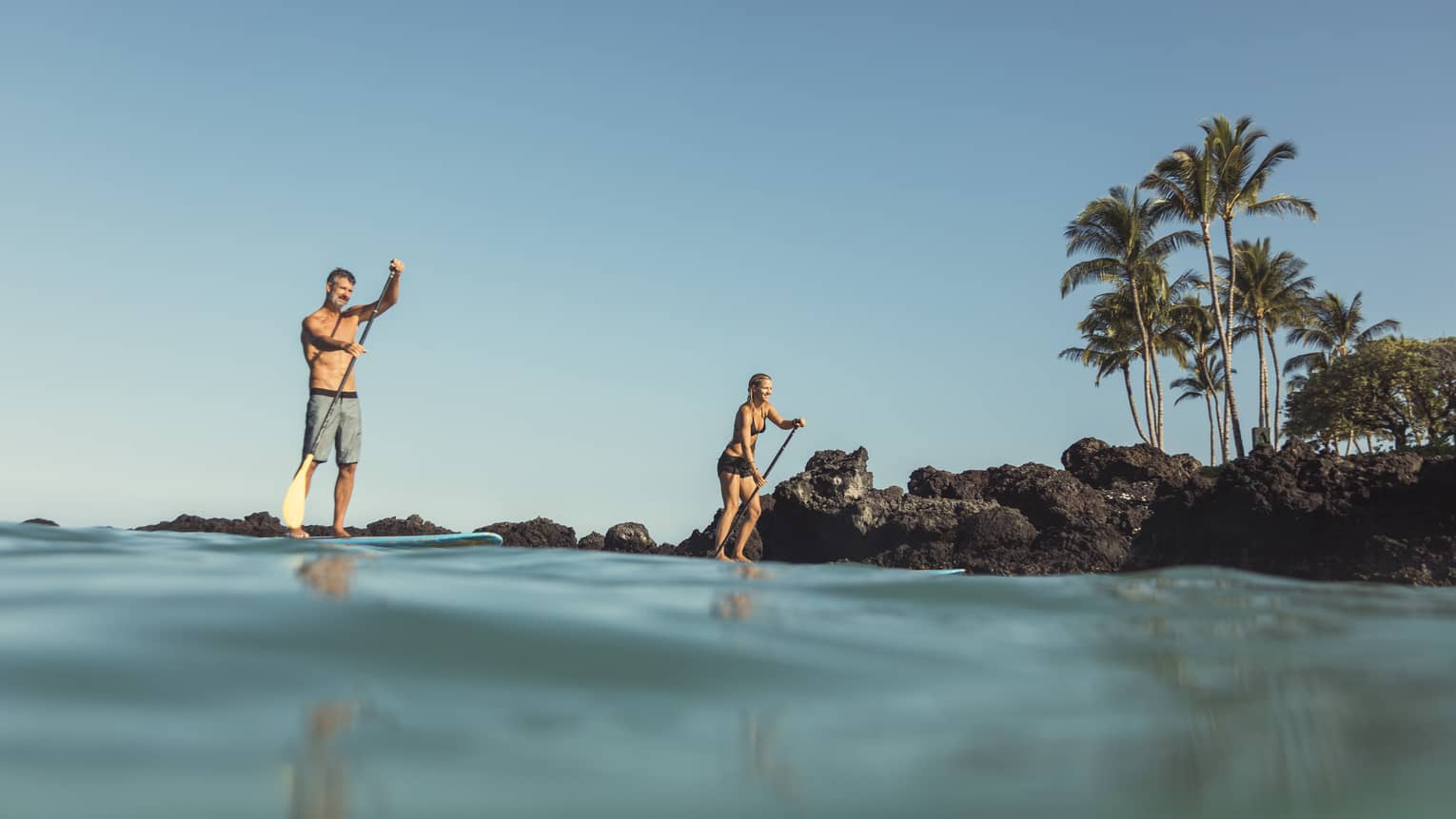 View from ocean looking up at two people on stand-up paddleboards near shore 