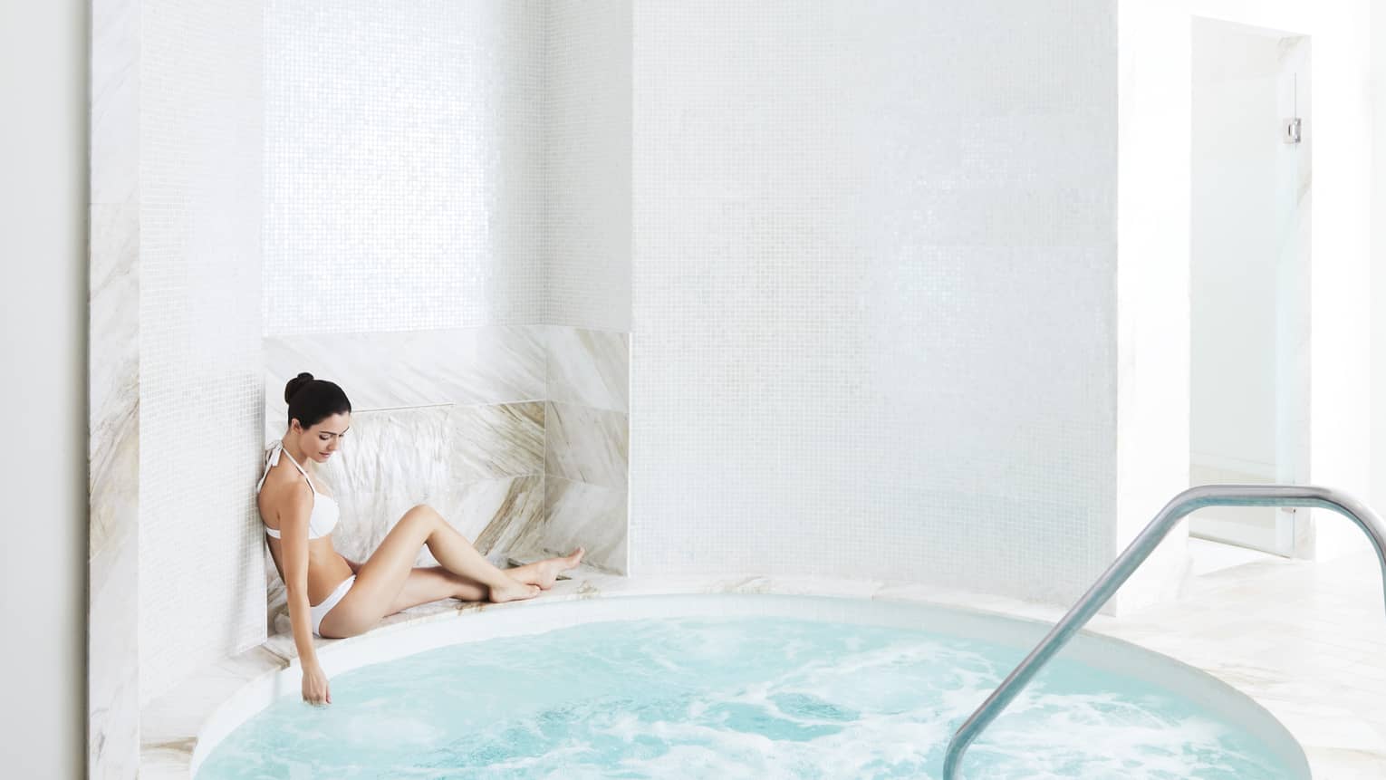 A woman relaxes by a marble hot tub in the spa