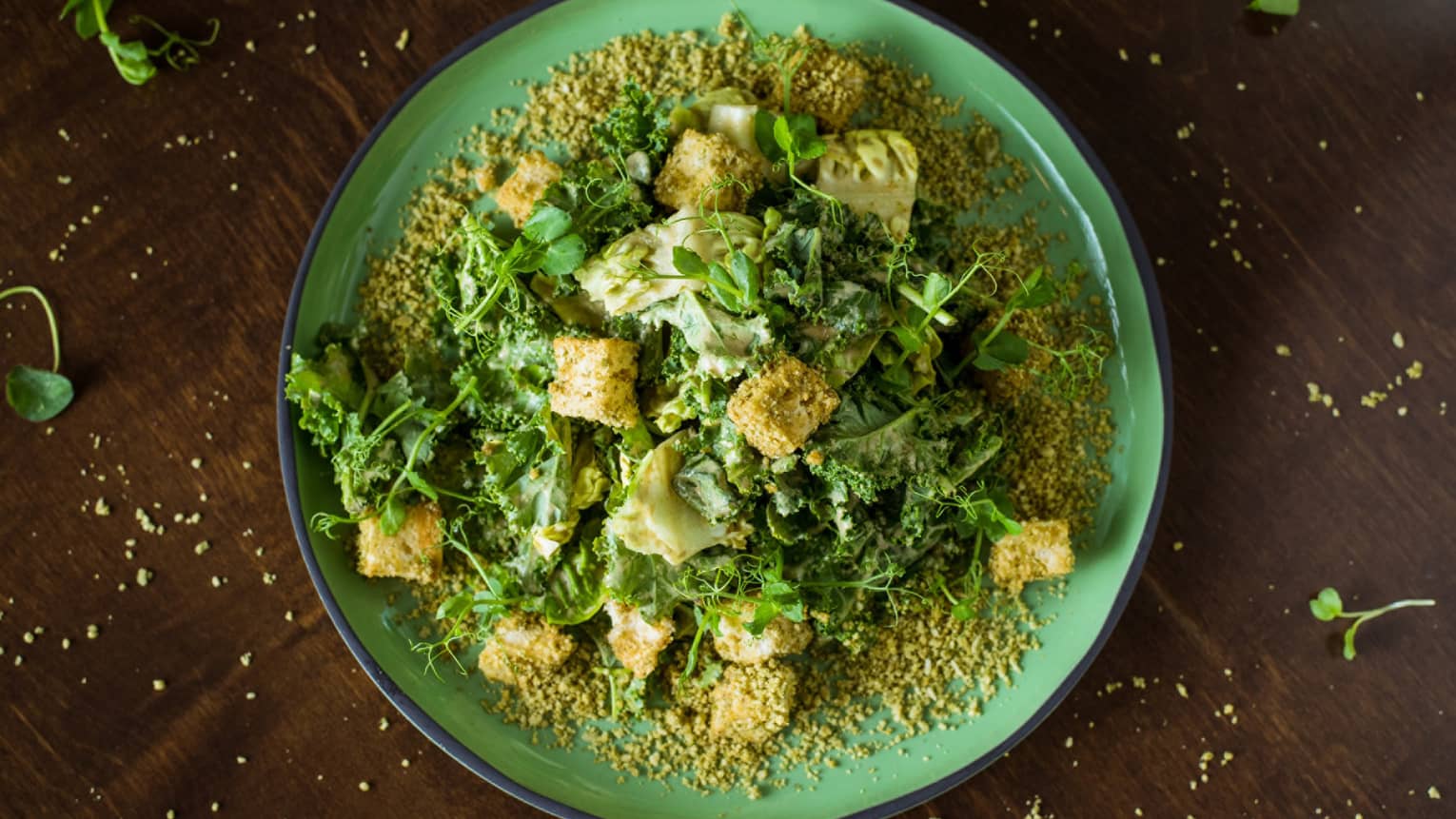 A salad covered with pumpkin seeds, served on a bright green plate.