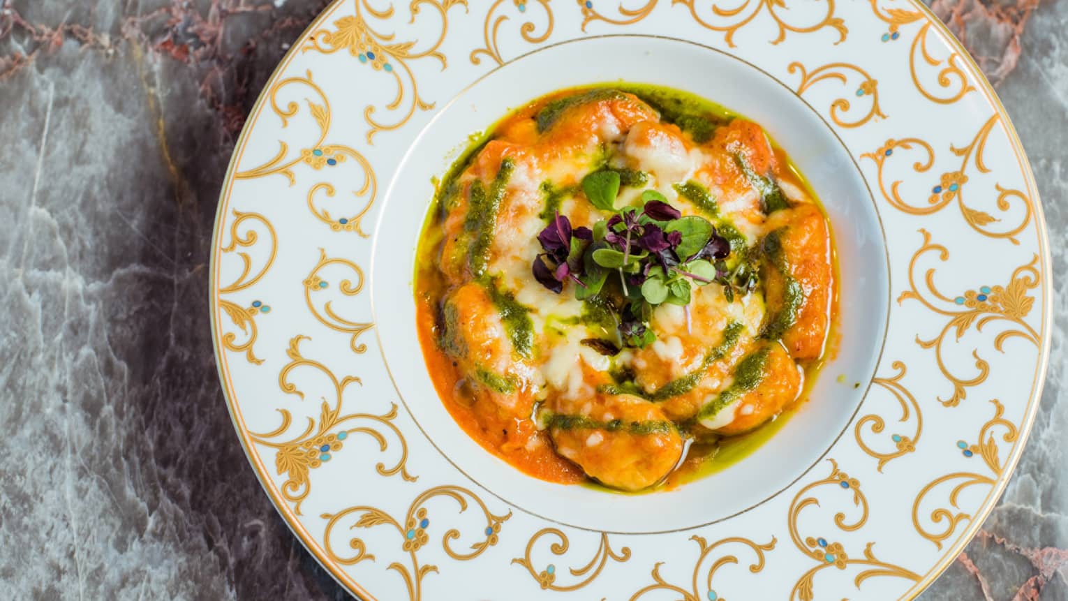 A white plate with golden accents, filled with an orange stew.