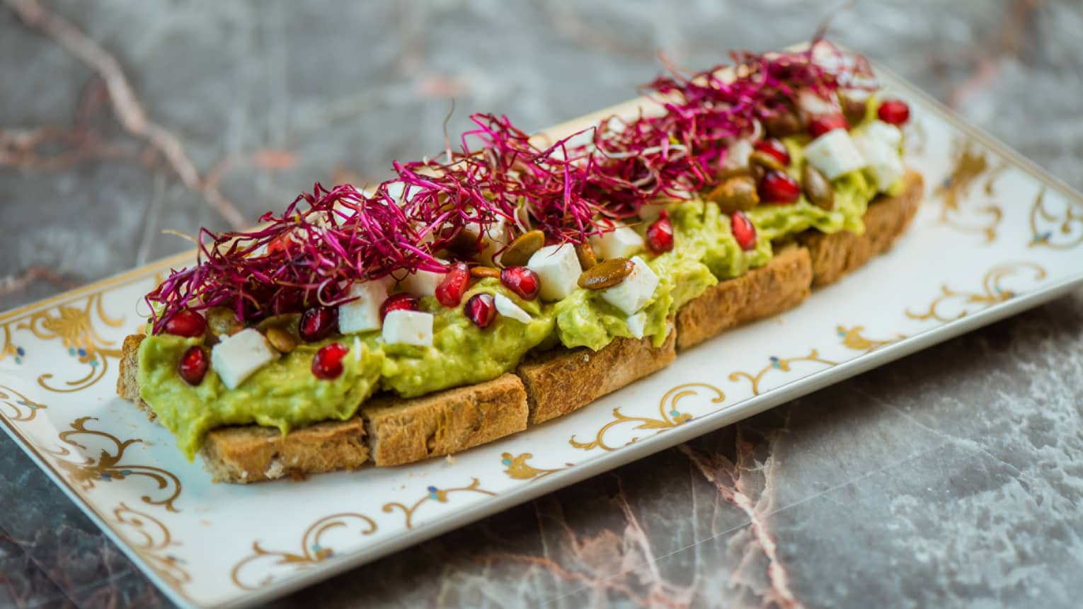 Toast topped with avocado, tomato, feta and pomegranate.