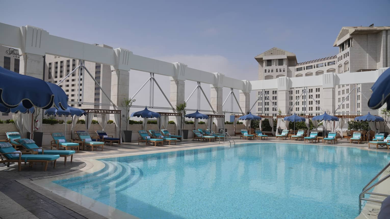 Outdoor rooftop pool surrounded by lounge chairs and a city skyline in the background