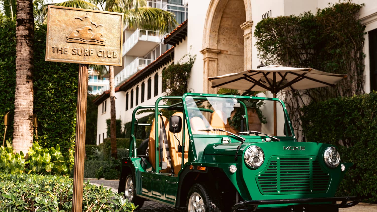 Green MOKE car parked outside of the building next to "The Surf Club" sign.