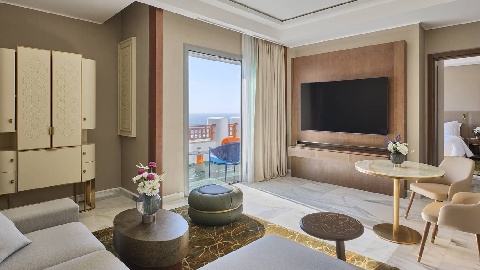 Four Seasons Executive Suite at Four Seasons Hotel Rabat, featuring a contemporary living room with a sofa, small round table and two chairs, walk-out, sea-view balcony, large hanging TV and separate bedroom