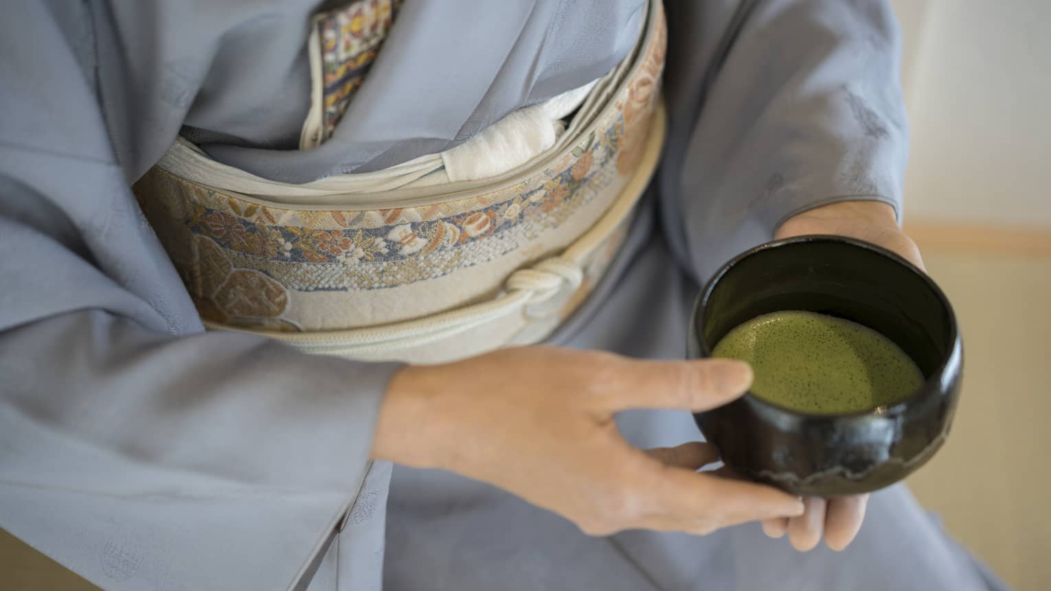 Close-up of woman in blue robe holding bowl with green matcha tea