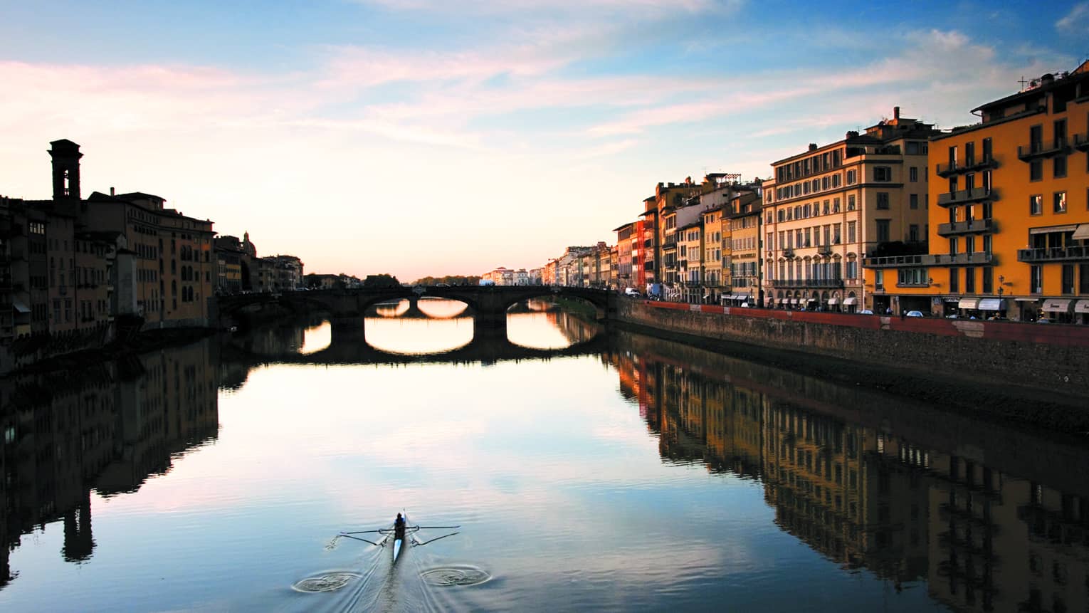 Person glides across canal in kayak under historic buildings
