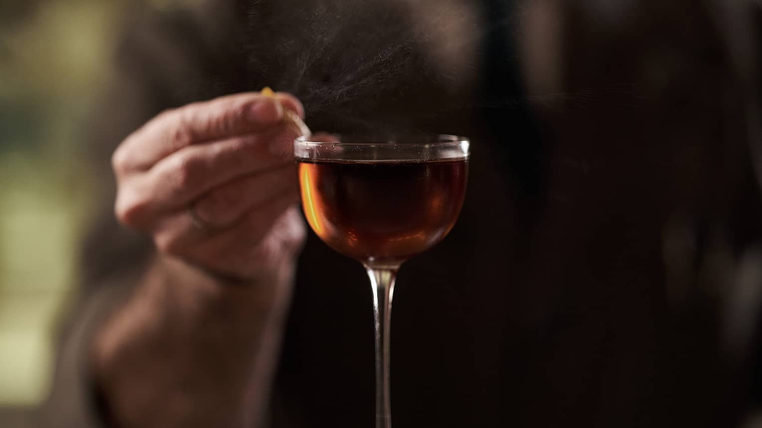 Bartender in suit garnishing a tall amber-coloured cocktail