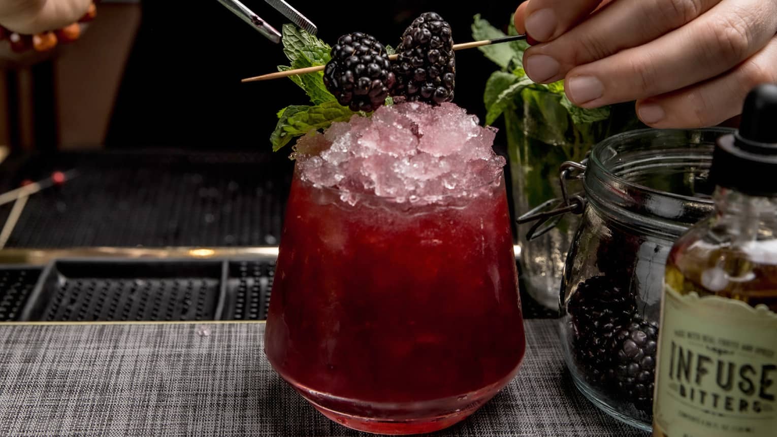 A bartender making a dark red cocktail with a berry garnish.