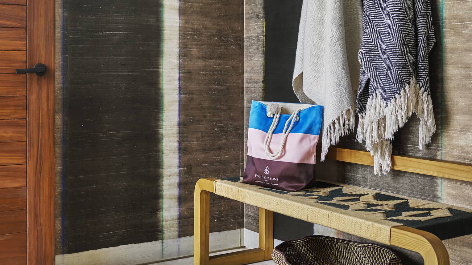 Resort room entryway with stylish wooden bench, shawls and hat hanging on wall hooks and a straw basket