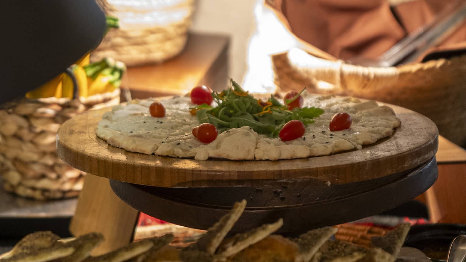 Cheese and za'atar manakeesh garnished with grape tomatoes and garnish on round cutting board