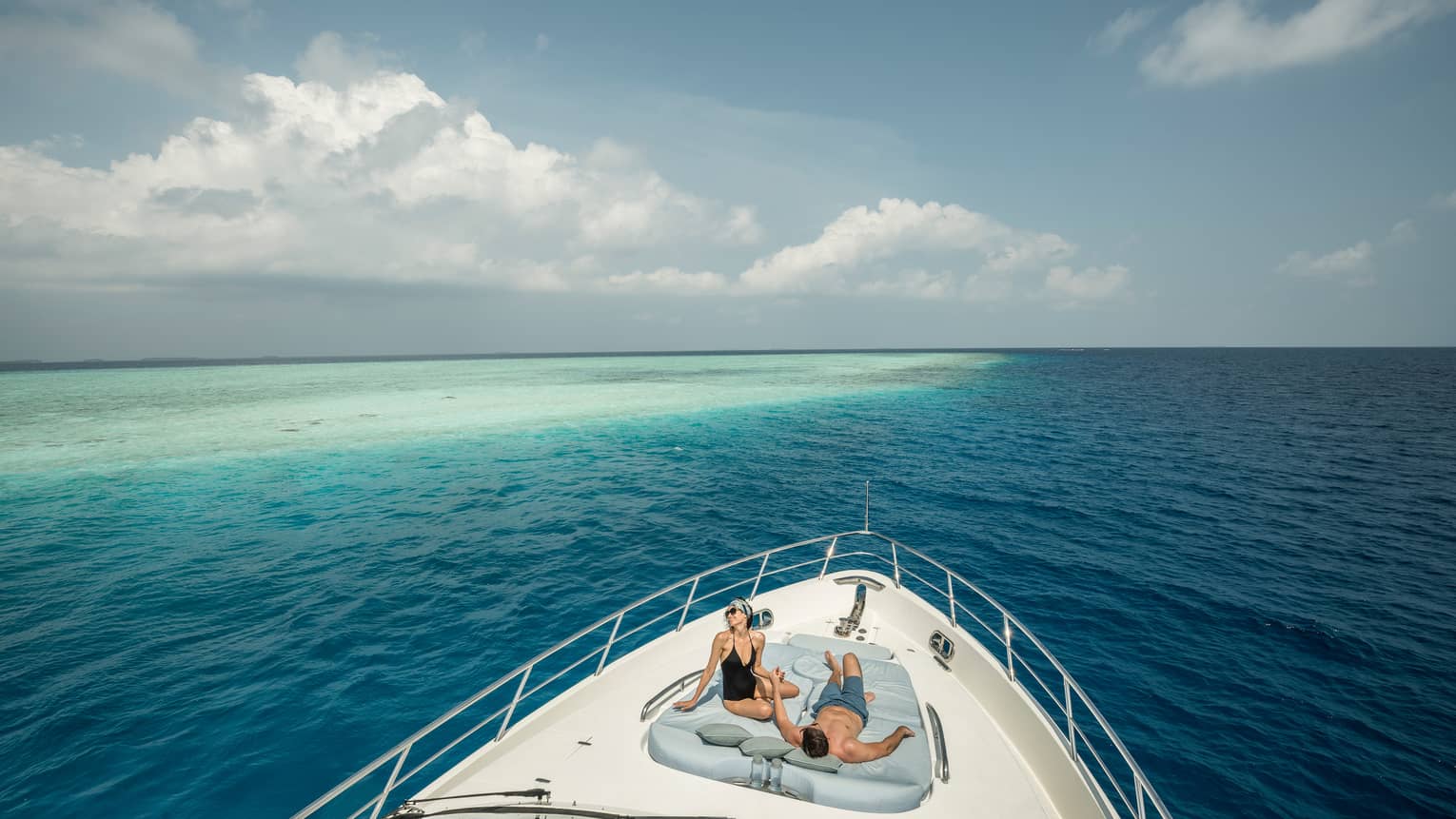 Couple lounge on cushions at front of Voavah Summer private yacht on ocean