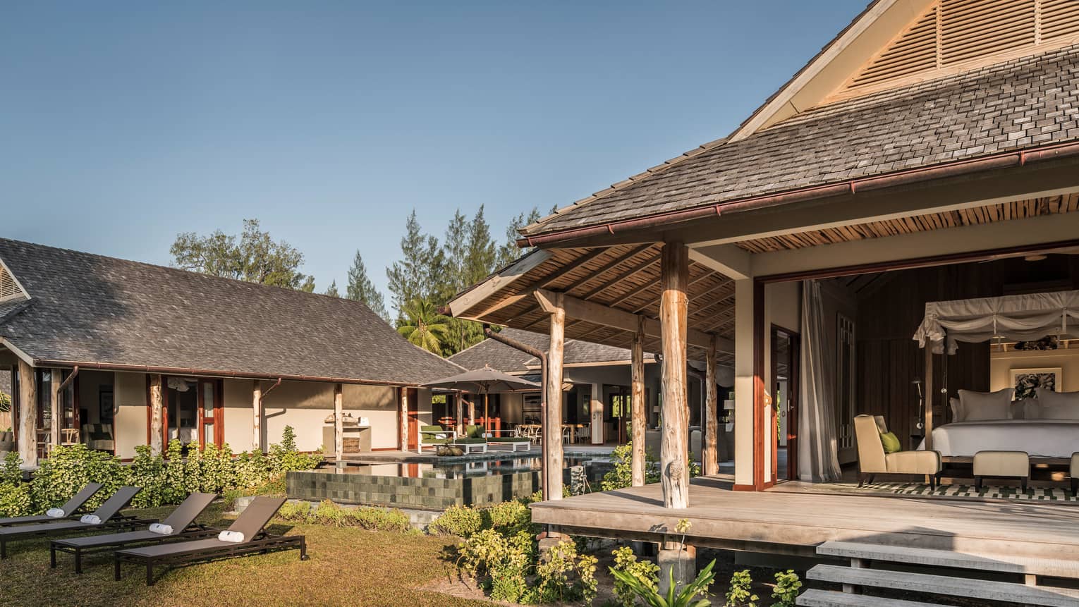 View of bungalow patio, open wall to bedroom from lawn with lounge chairs