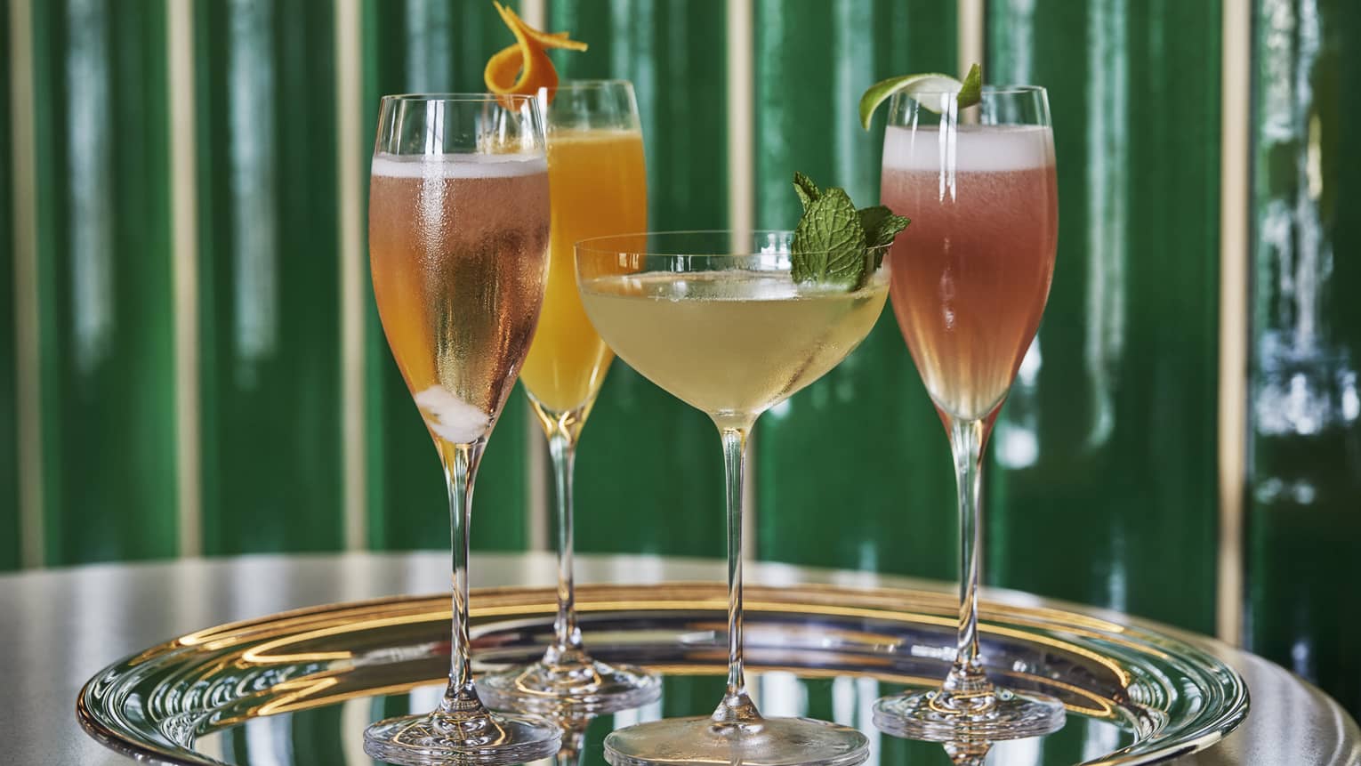 An tray of cocktails sit on a silver platter waiting to be served, green shinny background