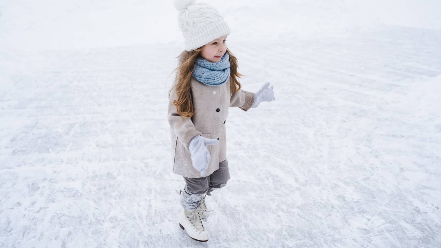 A small girl in winter clothes ice skating.