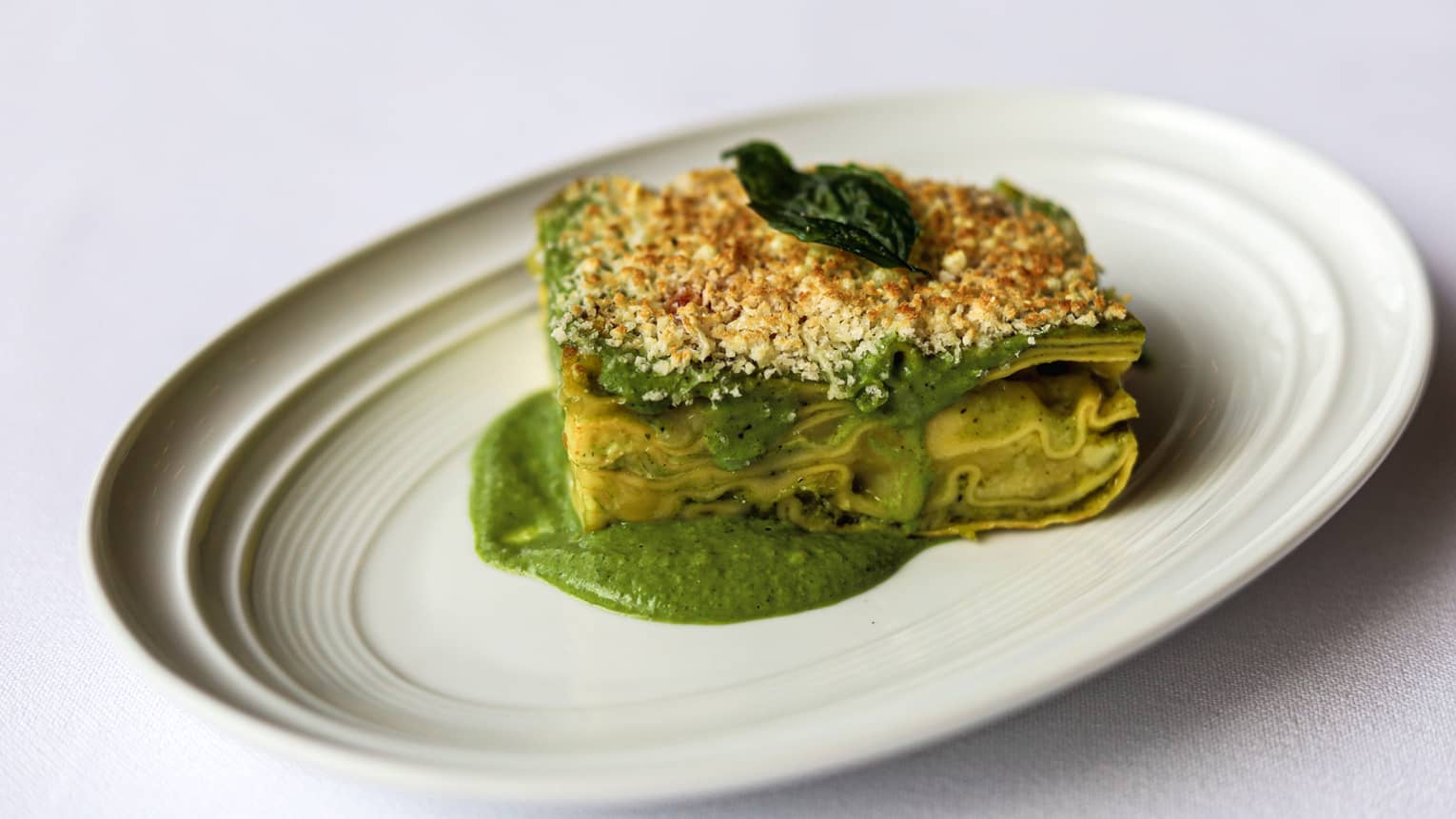 Fresh lasagna sheets layered with creamy pesto sauce gratinated with Parmigiano Reggiano on a white plate