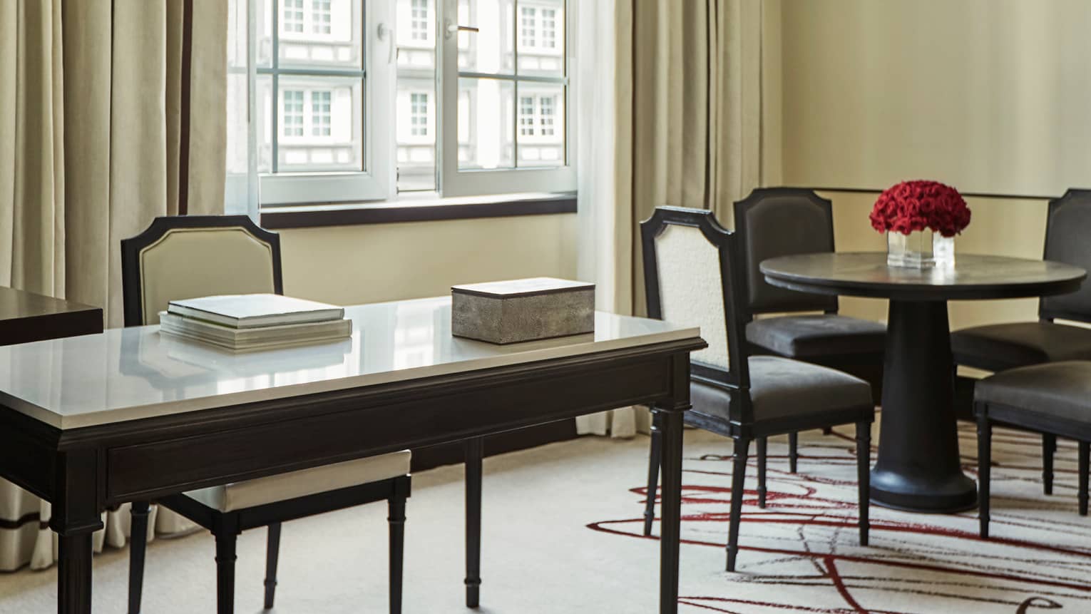 Hotel suite modern white desk, chair with books by cafe dining table with red roses, sunny window