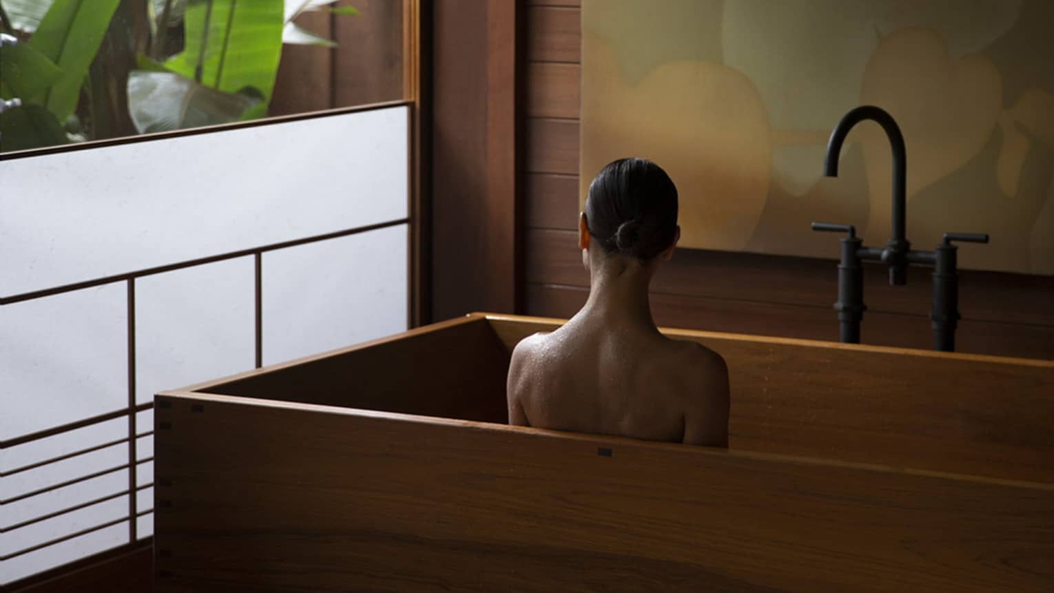 Woman sits in wooden, modern tub next to semi-frosted window