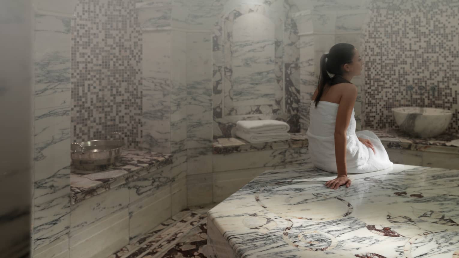 Back of woman in white towel on black-and-white marble ledge in Hammam steam room