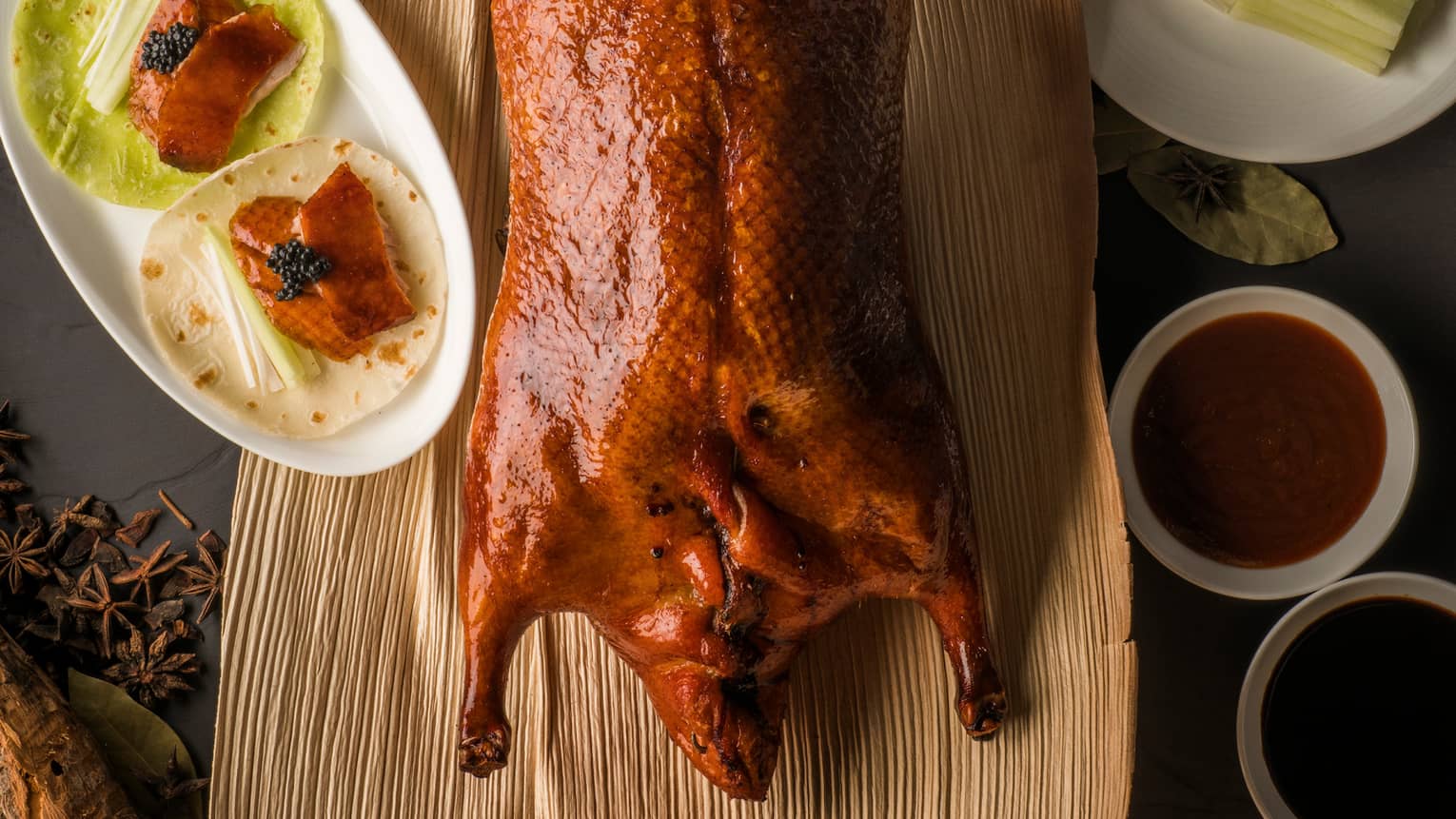Aerial view of whole Peking duck on wood platter beside small dishes with slices