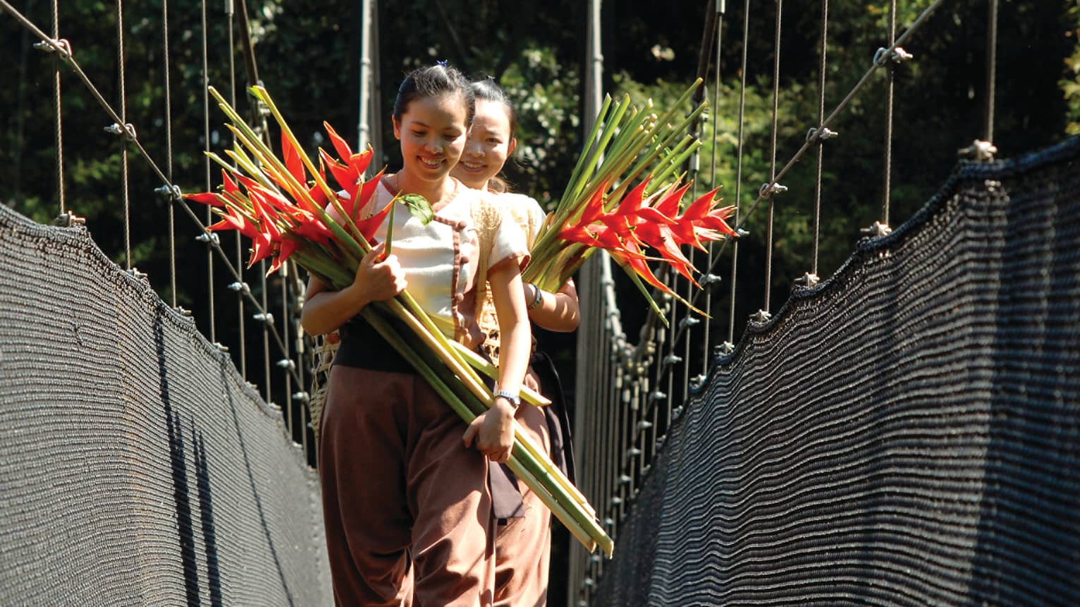 Two women walk down bridge holding bouquets of long-stemmed tropical flowers