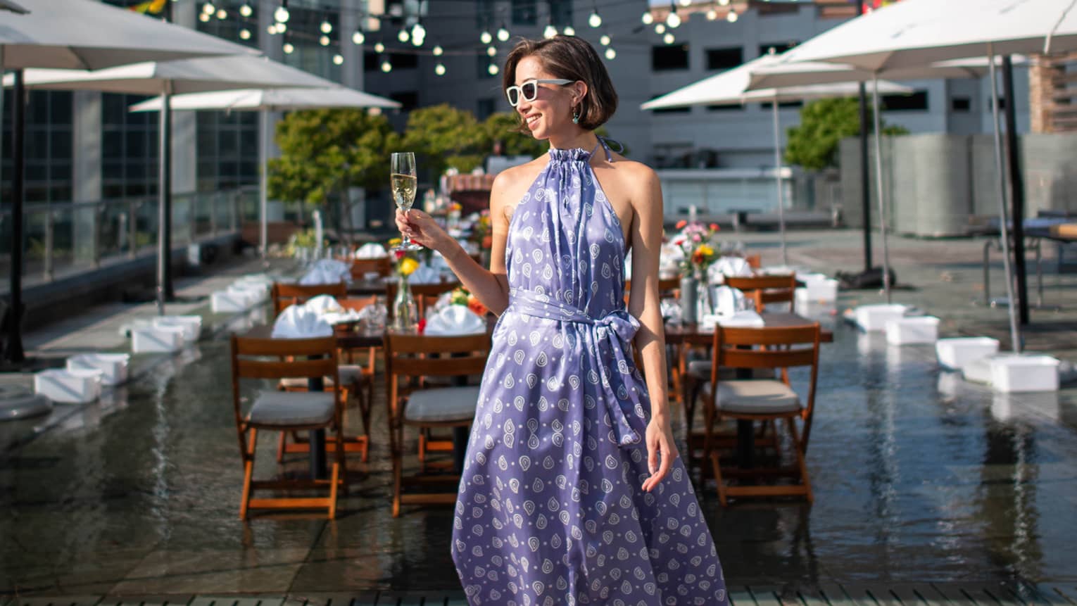 A person wearing a dress and standing on a rooftop terrace holding a glass of champagne