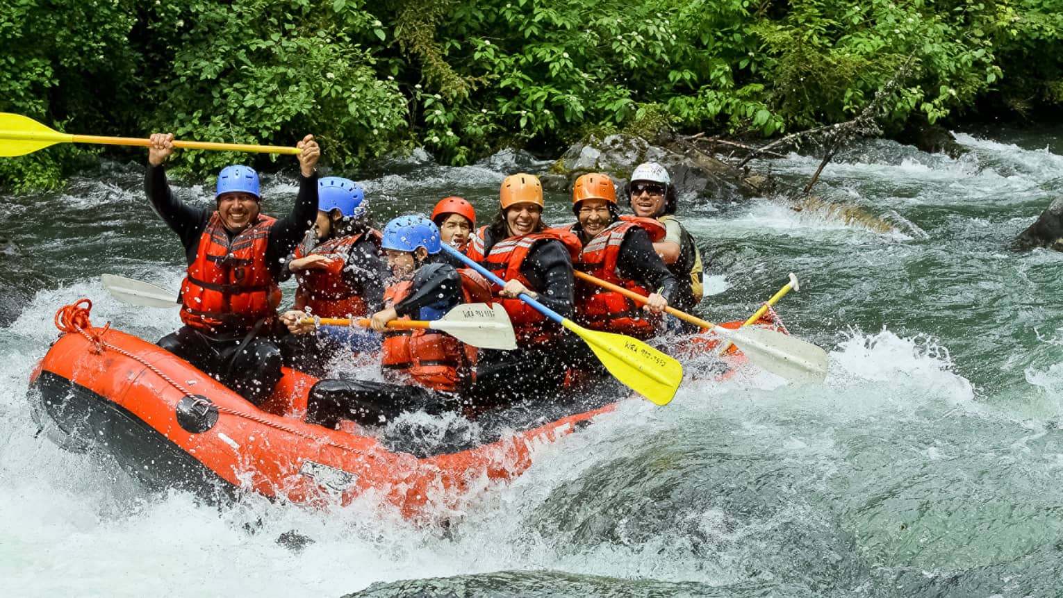 Smiling family wearing life jackets, helmets on white water raft on river rapids 