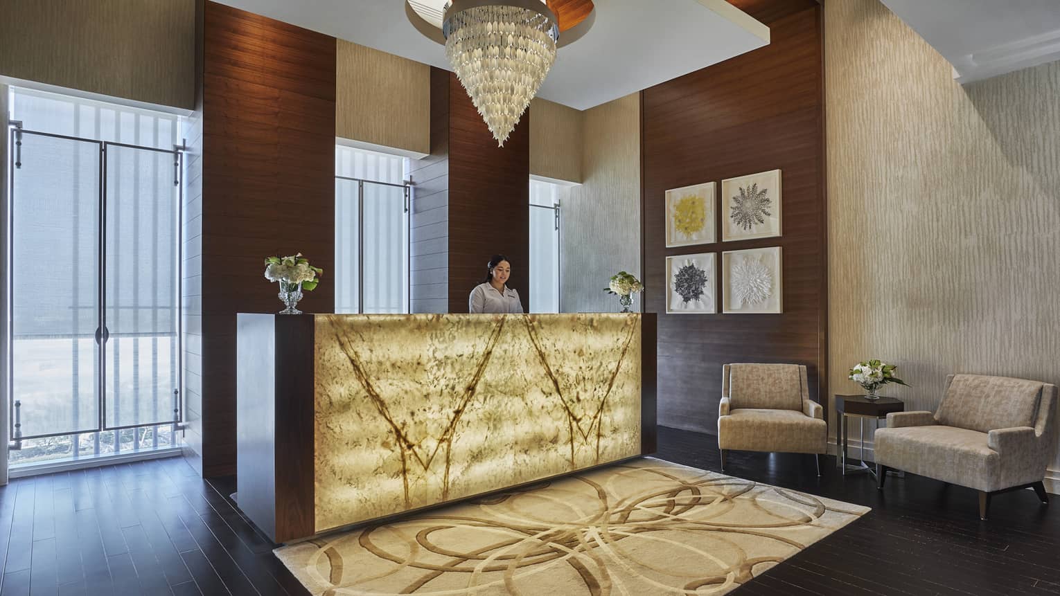 A yellow glass chandelier hangs over the welcome desk, adorned with soft yellow light and a brown rug. 