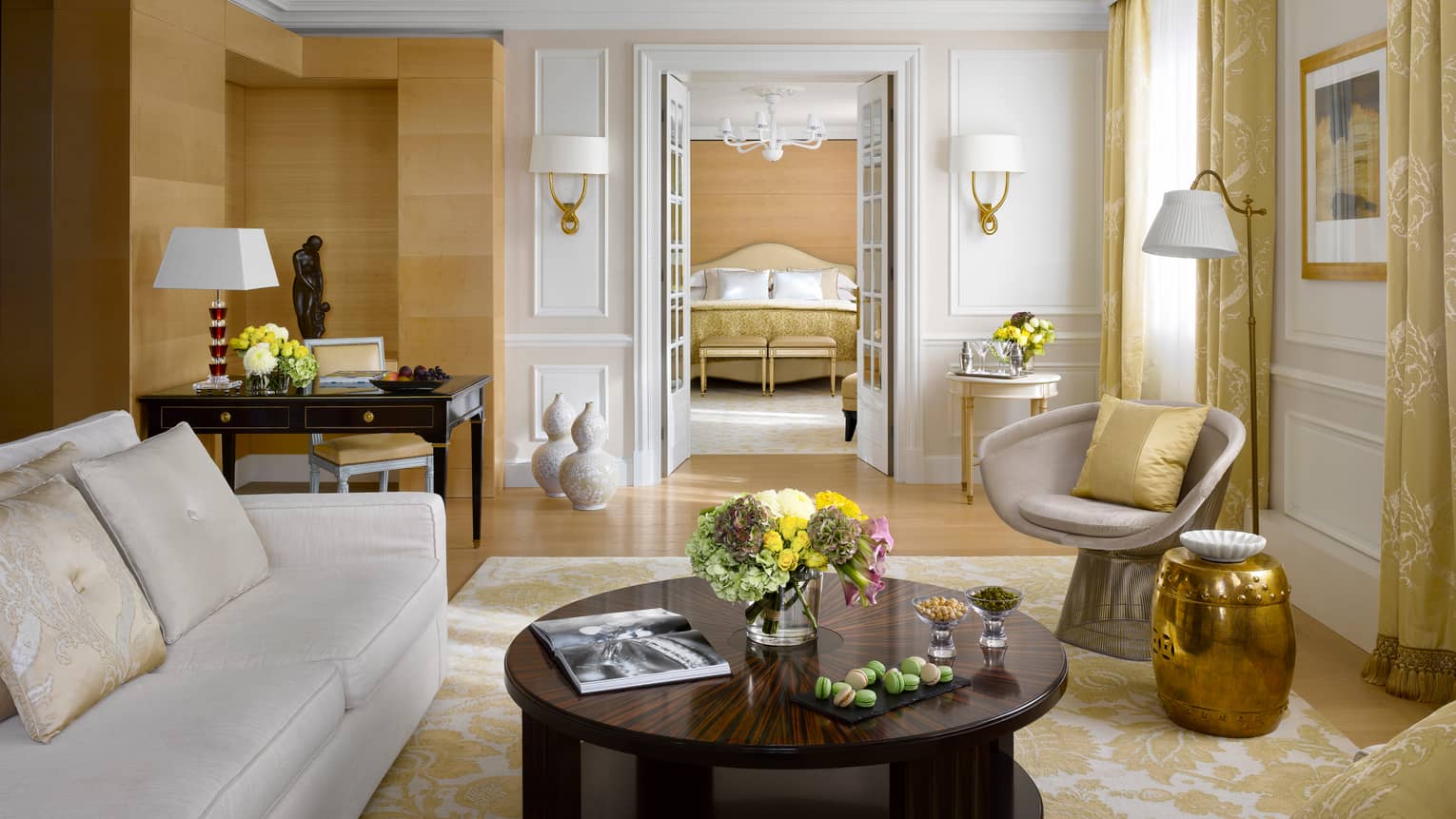 Presidential Suite Bergues room with white-and-gold decor, sofa, chair and round coffee table, French doors to bedroom