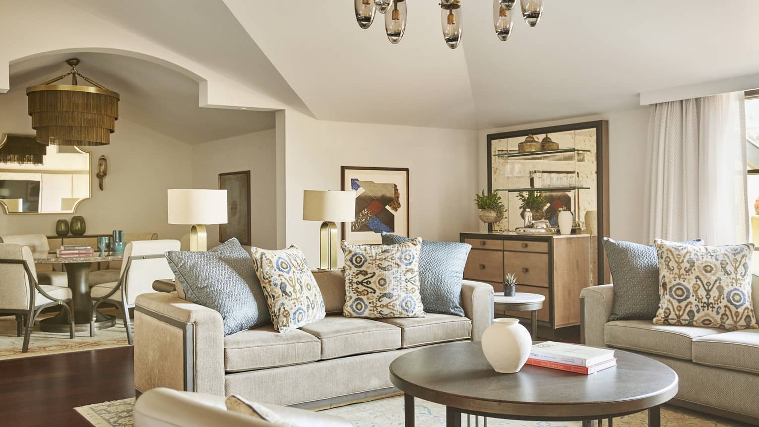 Hotel suite grey living area with round coffee table and neutral dining area in back