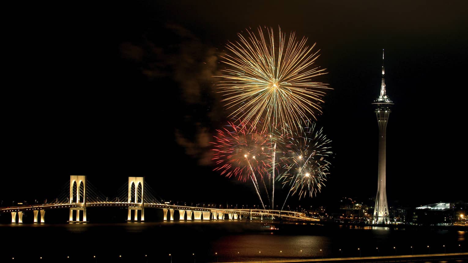 Fireworks against a black sky over bridge by Macau Tower 