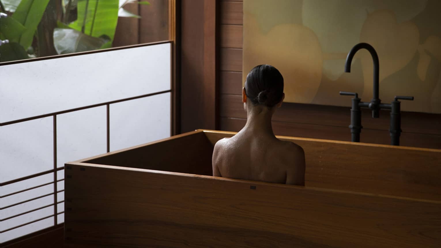 Woman sits in wooden, modern tub next to semi-frosted window