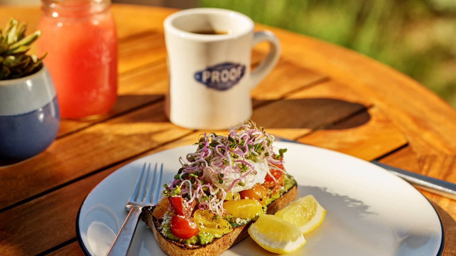Avocado toast with lemon on the side and a Proof mug.