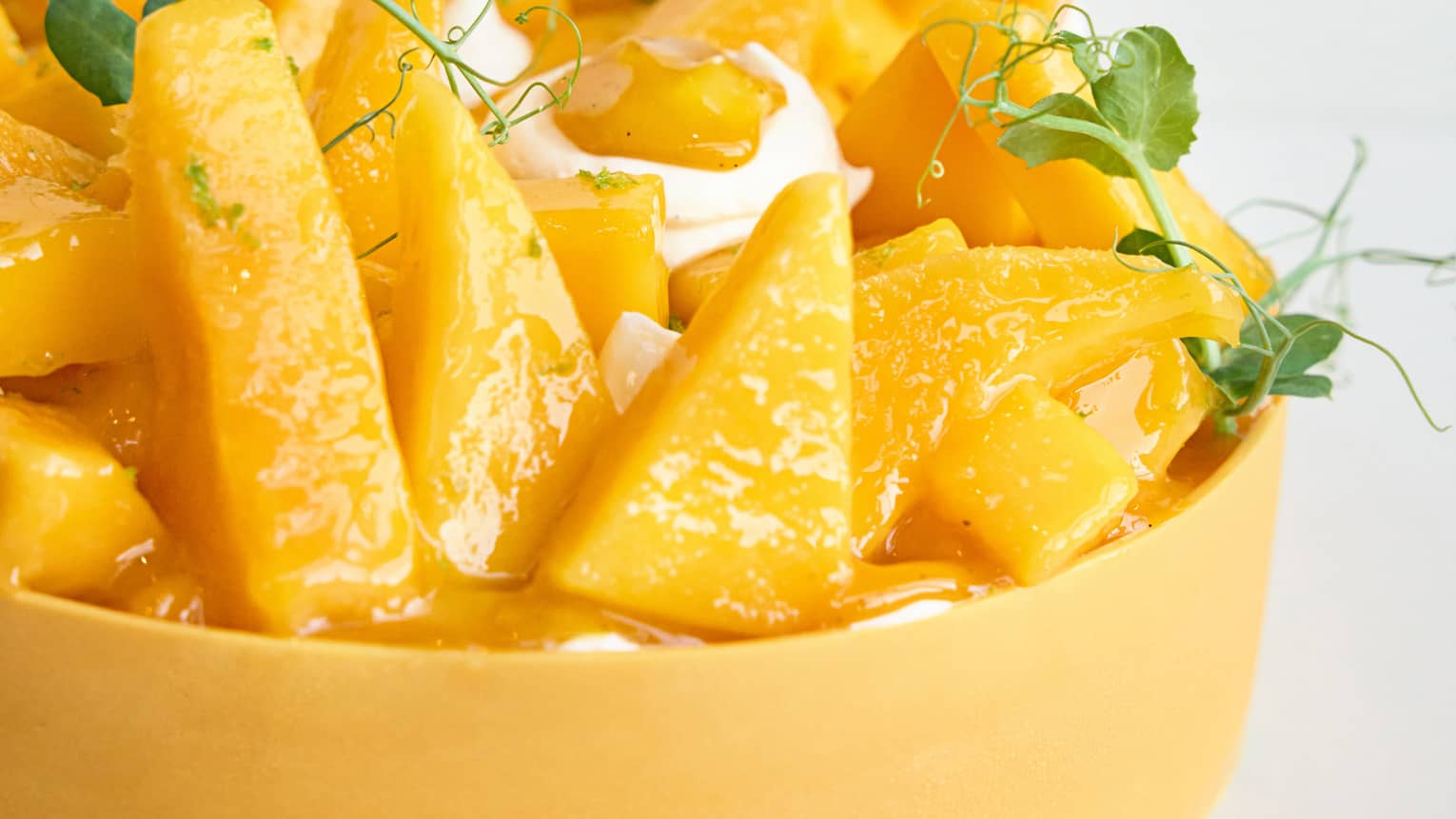 Round and yellow mango cheesecake topped with fresh mango slices, cream and sprigs of greenery