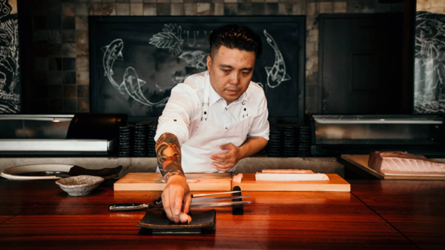 A male chef behind wooden counter places a piece of seafood on plate