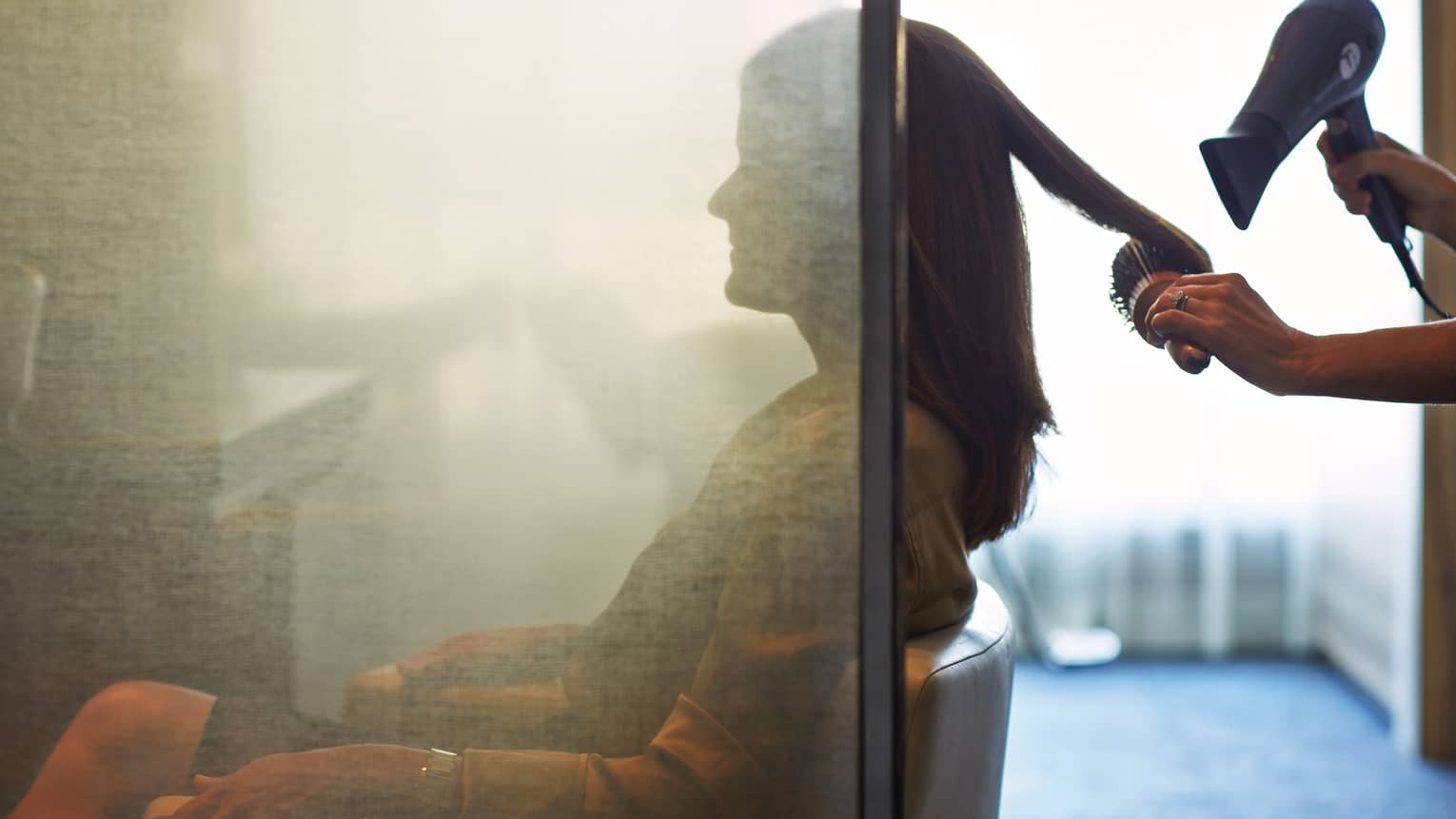 Silhouette of woman behind salon screen as hairdressers brushes, blow dries hair