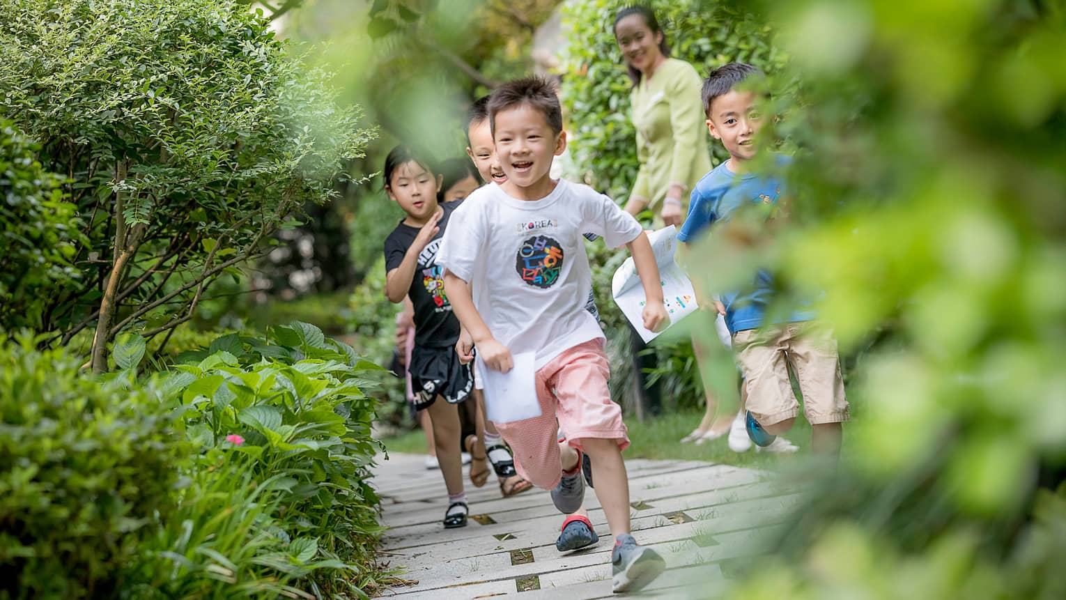 Smiling children run down wood path, bridge